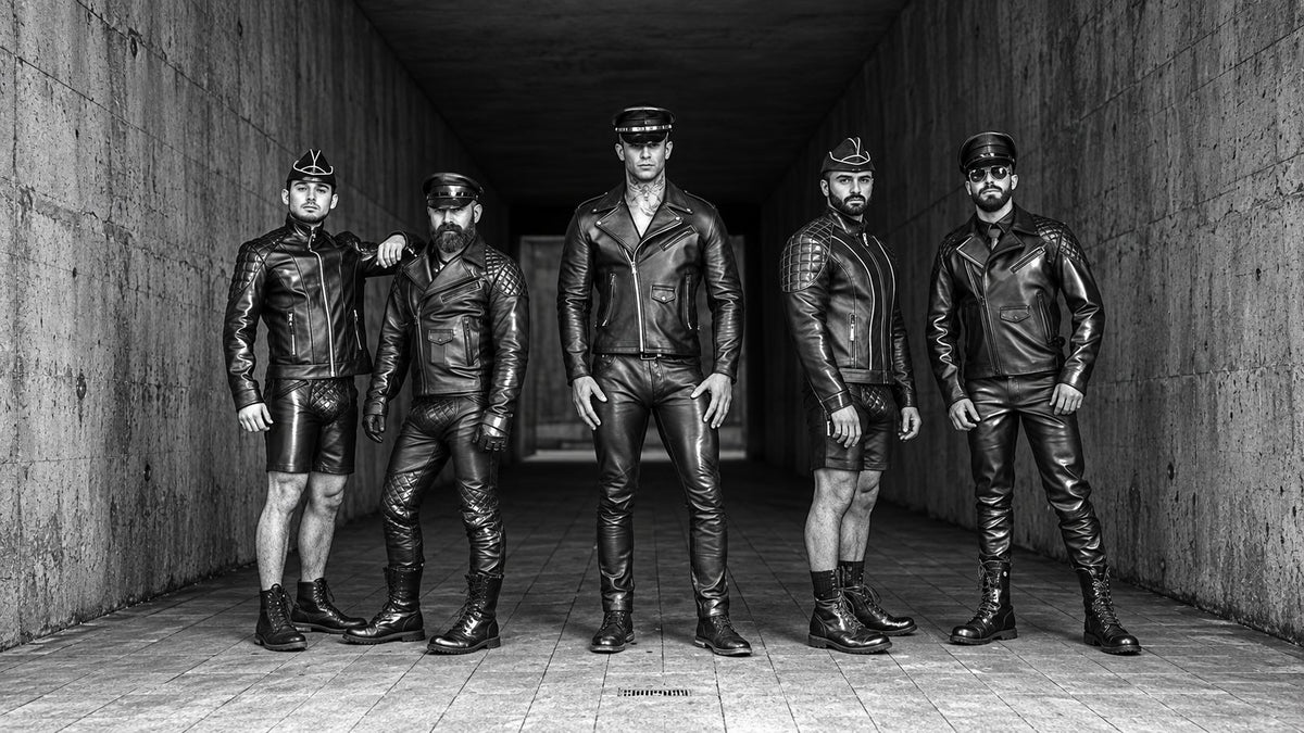 Five models in black leather jackets, caps and boots standing in a concrete corridor, in high-contrast black and white