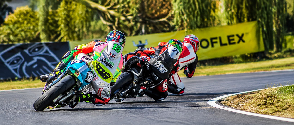 Three motorcycle racers leaning hard into a corner on a sunlit race track